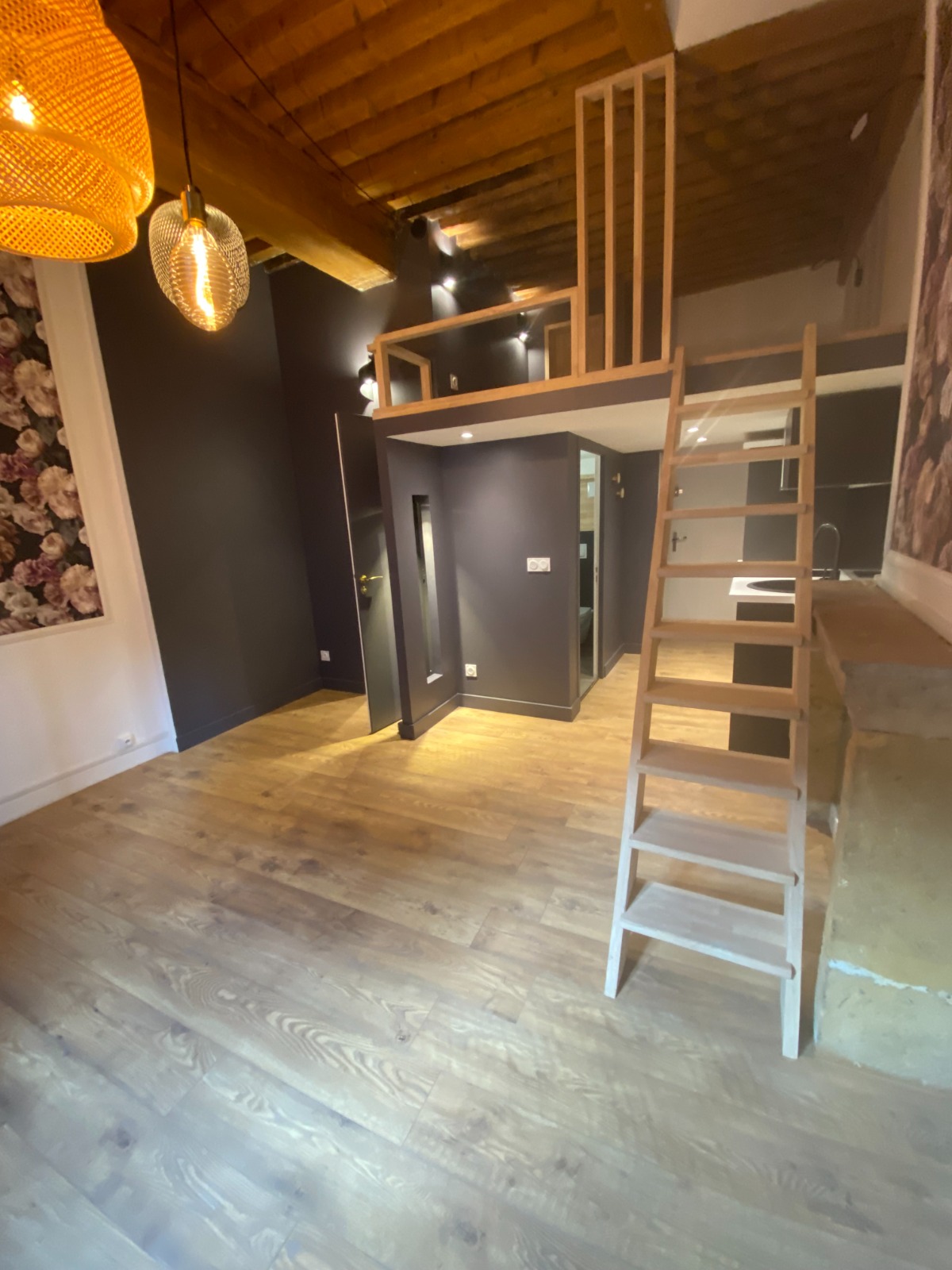 Studio avec mezzanine en bois, plafond à poutres apparentes et cloisons peintes gris anthracite sous la mezzanine